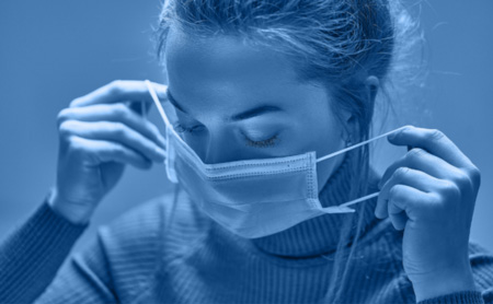 Woman putting on a PPE face mask, blue wash over image