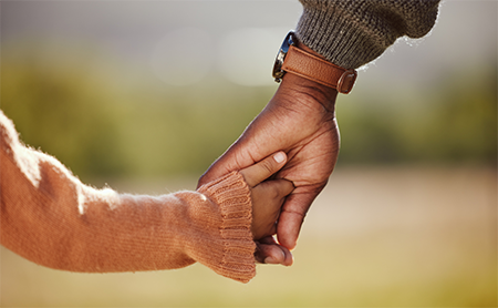 Adult holding a child's hand outdoors.