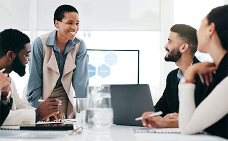 A woman leads a meeting with three colleagues seated around a table in a bright office.