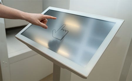 Close-up of a hand interacting with a kiosk displaying a hand icon.