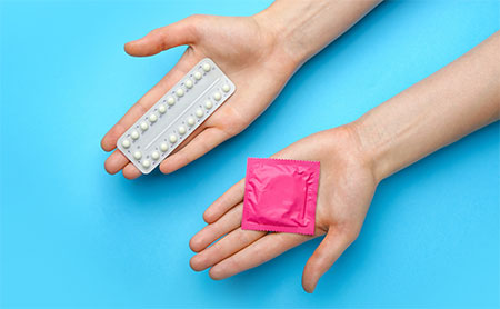 Hands open holding a condom and package of birth control pills.