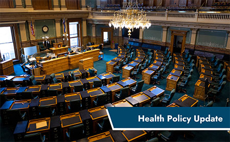 An empty legislative chamber with rows of desks and chairs, a central podium, and an American flag, overlaid with the text ‘Health Policy Update’.