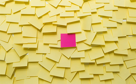 Yellow sticky notes covering a wall with one pink note at the center