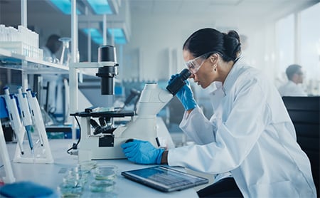 A scientist in a medical lab looks through a microscope