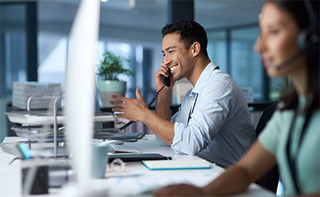 Office setting with a man on the phone and a woman in the background with a headset.